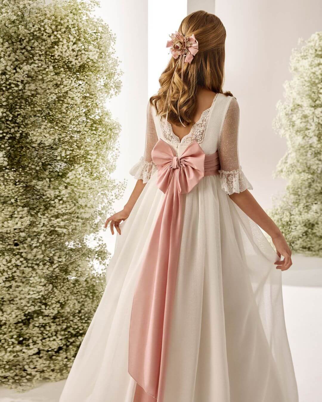 Vista posterior del vestido de Primera Comunión Rosa Clará First con espalda en V y gran lazo rosa - Modas y Confecciones Beatriz